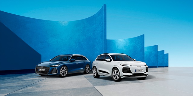 Zwei Audi-SUVs, ein weißes und ein blaues, stehen vor einer modernen, blau gestrichenen Wand mit geschwungenen Formen