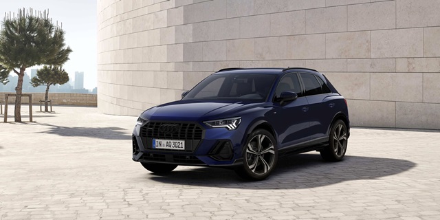 Blauer Audi Q3 in Frontansicht vor einer weißen Steinmauer.
