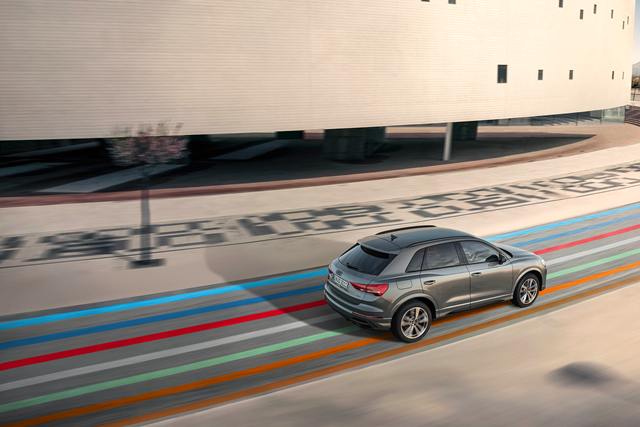 Audi Q3 fährt durch eine moderne Stadtstraße mit buntem Hahn Code.