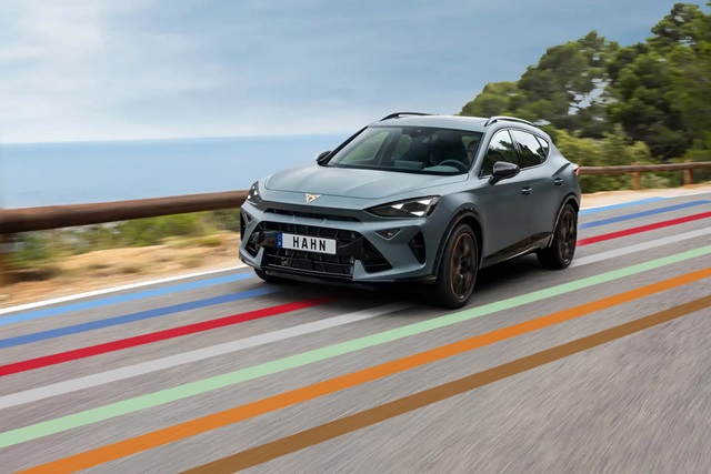 CUPRA Terramar VZ in Frontansicht in Fahrt auf einer Küstenstraße. Auf der Straße sind die bunten Linien des Hahn Codes abgebildet. 