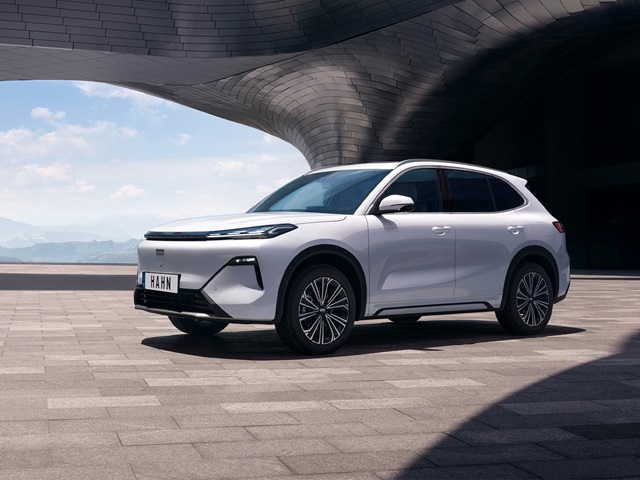 Geely Starry in weiß vor moderner Architektur mit geschwungenen Betonformen und blauem Himmel im Hintergrund