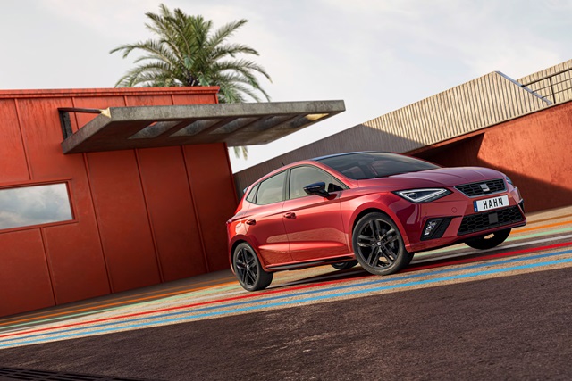 Roter SEAT Ibiza in Front-Seitenansicht parkend vor einem modernen Gebäude.