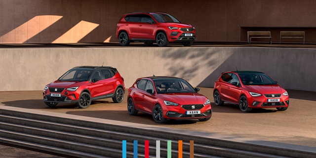 SEAT Leon, SEAT Ateca, SEAT Arona und SEAT Ibiza in rot parkend vor einem modernen Gebäude. Drei der Modelle stehen auf einer Ebene vor einer Wand, ein Modell dahinter etwas erhöht auf einer zweiten Ebene.