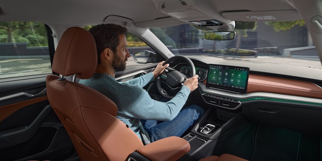 Ein Mann sitzt am Steuer eines Škoda und hat beide Hände am Lenkrad.
