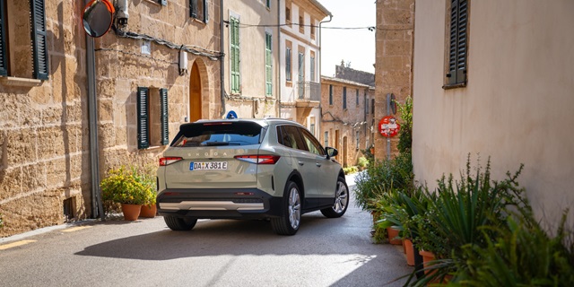 Heckansicht eines Škoda Elroq in Timiano-Grün in einer engen Gasse mit mediterranen Gebäuden und Pflanzen in Töpfen