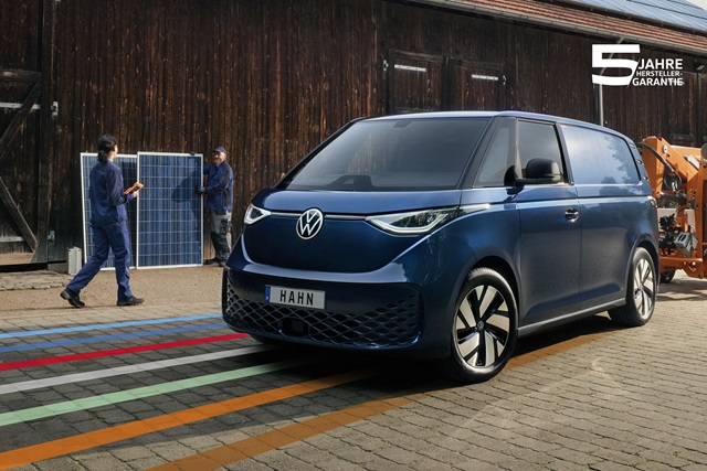 Ein blauer Volkswagen ID. Buzz Cargo mit Handwerkern im Hintergrund, die Solarpaneele installieren.