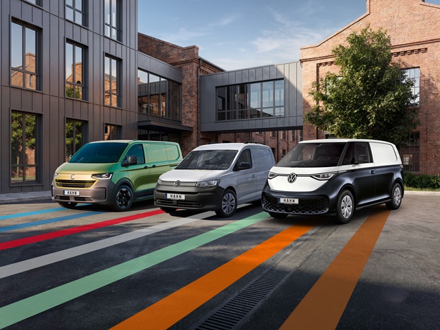 Drei nebeneinander geparkte Volkswagen Nutzfahrzeuge vor einem modernen Backsteingebäude von links nach rechts: ein Transporter, ein Caddy und ein ID. Buzz