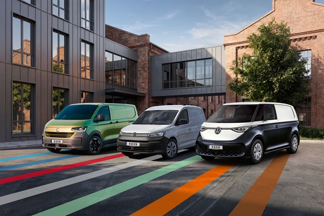 Drei nebeneinander geparkte Volkswagen Nutzfahrzeuge vor einem modernen Backsteingebäude von links nach rechts: ein Transporter, ein Caddy und ein ID. Buzz