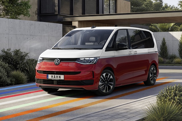 VW Multivan eHybrid in Rot und Weiß als Seitenansicht vor modernem Haus mit Betonfassade und Pflanzen