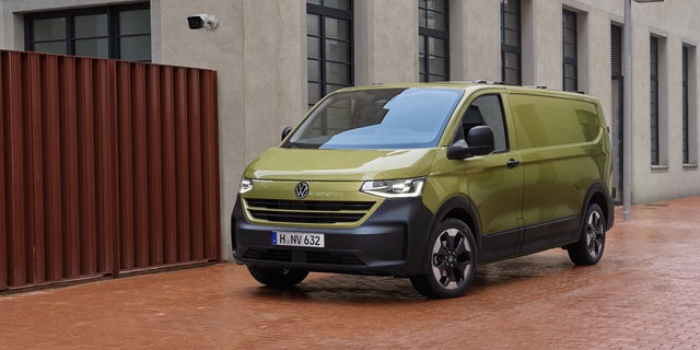 Grüner Volkswagen Transporter Kastenwagen, geparkt auf einer Ziegelsteinstraße vor einem modernen Gebäude.