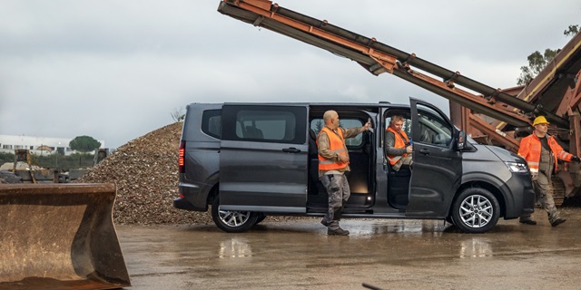 Drei Bauarbeiter befinden sich um den Volkswagen Transporter Kastenwagen Kombi, der mit geöffneter Schiebetür parkt. Der Transporter steht auf einer Baustelle, die man im Hintergrund erahnen kann.