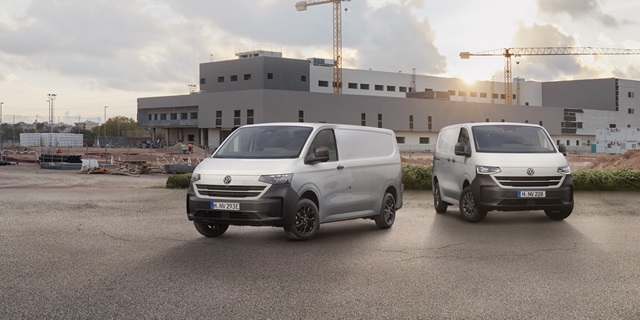 Zwei Modelle des neuen Volkswagen Transporter Plus vor einem Gebäude und einer Baustelle, die im Hintergrund zu sehen sind.