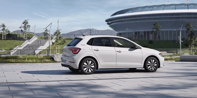 Ein weißer Volkswagen Polo GOAL in Seitenansicht auf einem Parkplatz vor einem Stadion, das man im Hintergrund erkennen kann. 
