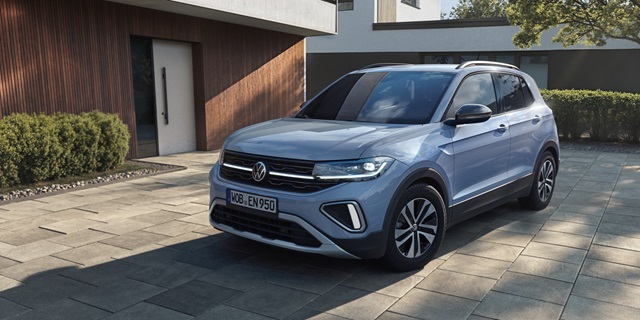 Glaublauer Volkswagen T-Cross ENERGY auf einem Parkplatz vor einem modernen Haus.
