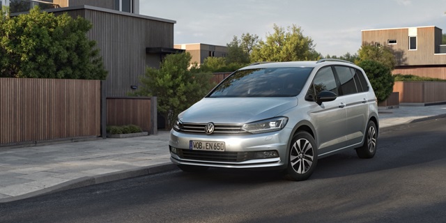 Ein silberner VW Touran in Fronansicht parkend am Straßenrand.