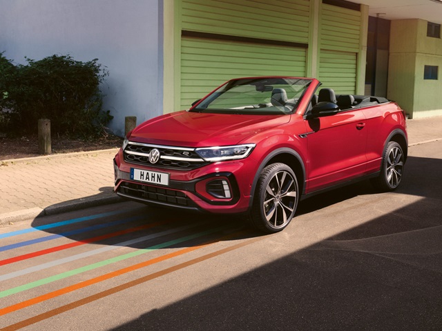 Rotes VW T-Roc Cabriolet am Straßenrand vor grünen Gebäude.