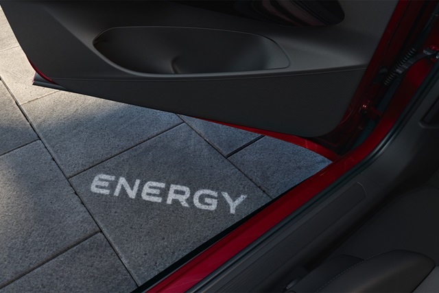 Das geöffnete Autotürinnere wirft das Wort 'ENERGY' als Lichtprojektion auf den Boden aus grauen Pflastersteinen