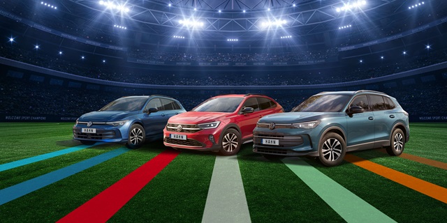 VW Golf Variant, Taigo und Tiguan in Blau, Rot und Grau stehen nebeneinander auf einem Fußballfeld unter Flutlicht in einem Stadion.