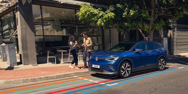 Der VW ID.4 in blau parkend am Straßenrand. Unter dem Auto gehen bunte Streifen entlang.