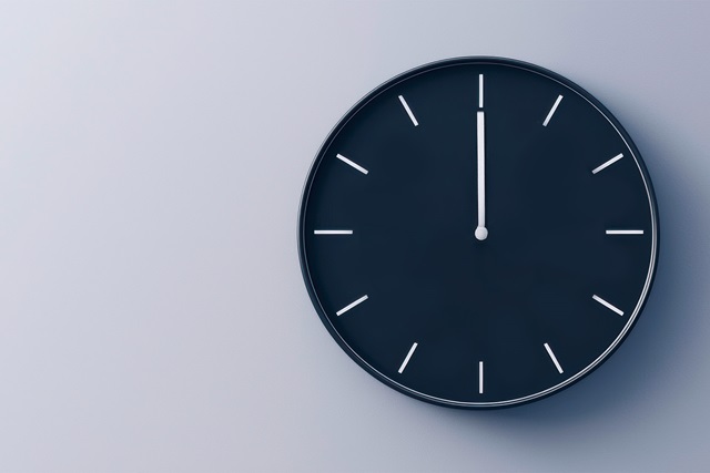 Eine Dunkelblaue Uhr auf hellblauem Hintergrund. Die Uhr hat weiße Zeiger, die 12 Uhr anzeigen.