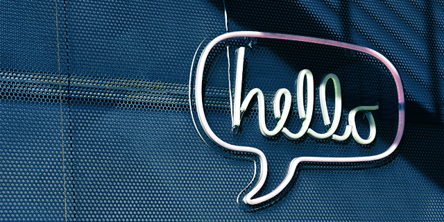 Schild in Form einer Sprechblase mit dem Wort 'hello' an einer dunklen Wand