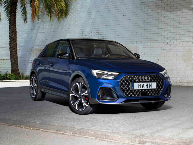 Blauer Audi A1 Allstreet mit auffälligem Wabengrill steht vor einer weißen Backsteinmauer neben Palmen