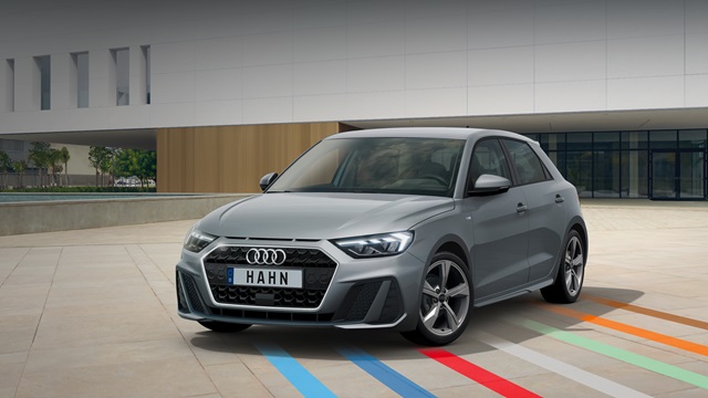 Grauer Audi A1 in Frontansicht auf gepflastertem Platz mit farbigen Linien vor modernem Gebäude