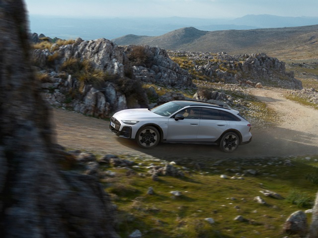 Weißer Audi A6 Allroad Hybrid fährt auf einem unbefestigten Gebirgsweg mit felsigem Gelände im Hintergrund