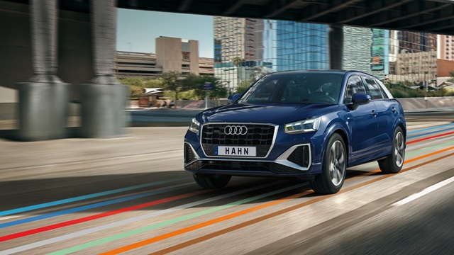 Blauer Audi Q2 fährt in Frontansicht auf einer Straße unter einer Brücke in urbaner Umgebung