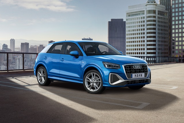 Blauer Audi Q2 in Seitenansicht auf Parkdeck mit Hochhauskulisse
