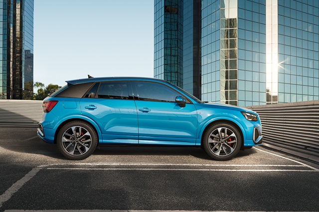 Hellblauer Audi Q2 in Seitenansicht vor modernen Glasgebäuden auf einem Parkplatz
