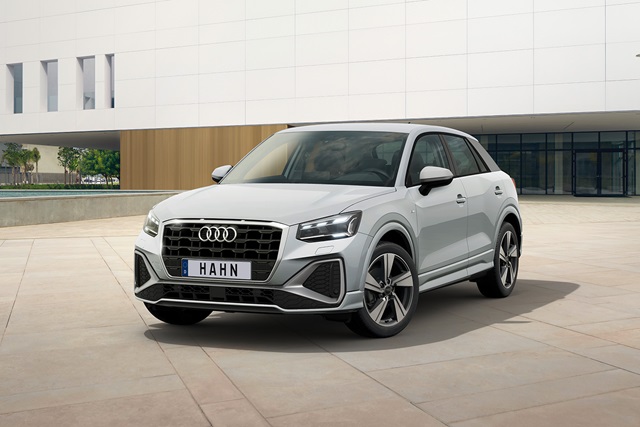 Silberner Audi Q2 in Frontansicht vor modernem Gebäude mit großem Fenster und Holzverkleidung