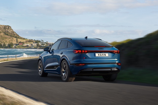 Blauer Audi Q6 e-tron Sportback Rückansicht auf kurviger Küstenstraße mit Landschaft im Hintergrund.