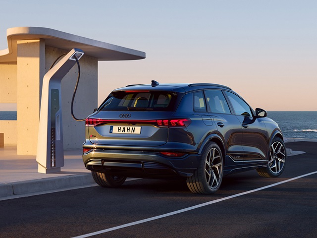 Audi Q6 SUV e-tron beim Laden an einer Ladestation am Strand, in der Abenddämmerung.