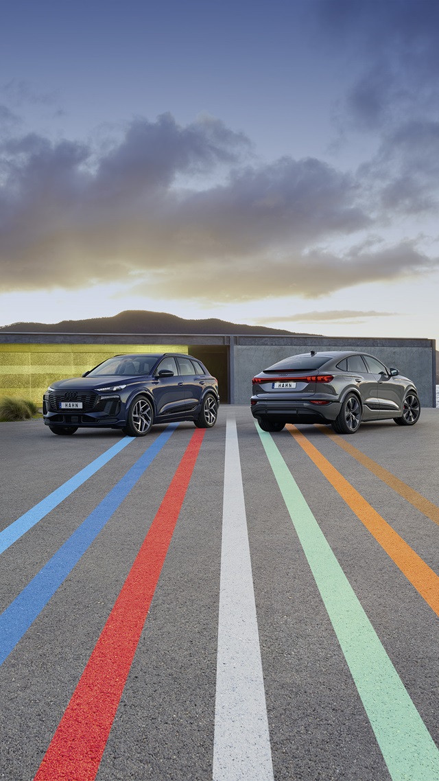 Zwei Audi Q6 e-tron SUV und Sportback nebeneinander auf einer Straße mit farbigen Streifen im Vordergrund