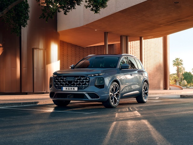Blauer Audi Q7 SUV in Frontansicht vor modernem Gebäude mit Säulen und Palmen im Hintergrund
