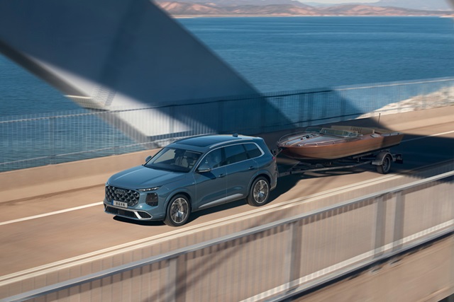 Blauer Audi Q7 zieht auf einer Brücke einen Anhänger mit einem Boot