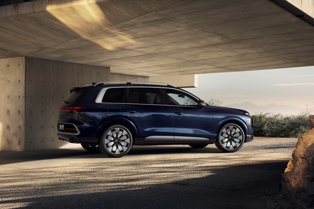 Seitliche Ansicht eines blauen Audi Q9 SUV vor einer modernen Betonarchitektur mit Berglandschaft im Hintergrund