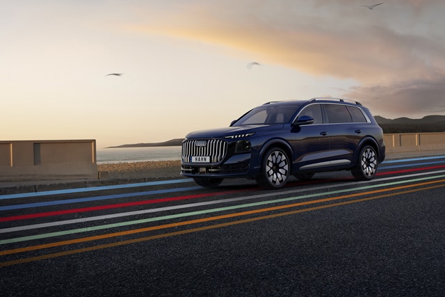 Seitenansicht eines blauen Audi Q9 SUV auf einer Straße mit farbigen Linien und einem Himmel bei Sonnenuntergang