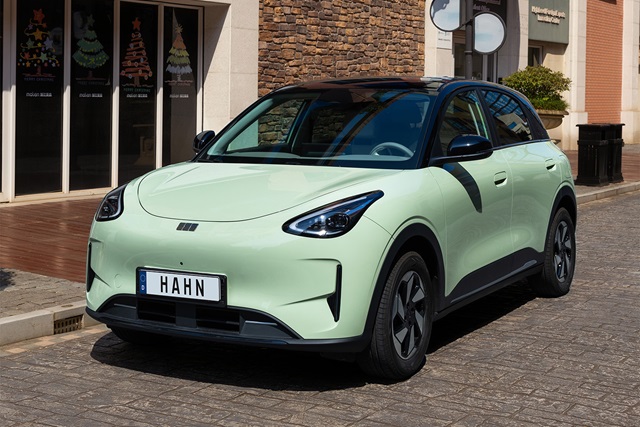 Geely E2 in Mintgrün aus schräger Frontansicht mit sichtbarem Kennzeichen 'HAHN' auf gepflasterter Straße vor Gebäuden.