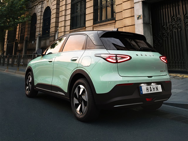 Schräge Rückansicht des minigrünen Geely E2 auf einer Straße vor einem alten hellbraunen Gebäude