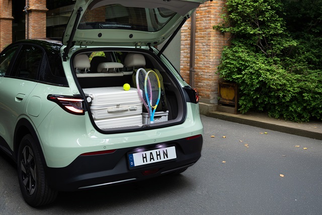 Offener Kofferraum eines mintfarbenen Geely E2 mit zwei Tennisschlägern, einem Tennisball und einem weißen Koffer