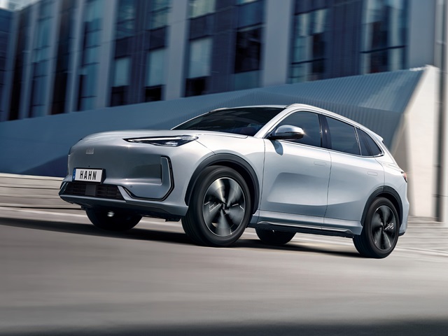 Weiße Seitenansicht eines Geely E5 SUV mit schwarzem Dach und modernen Felgen vor einem modernen Gebäude