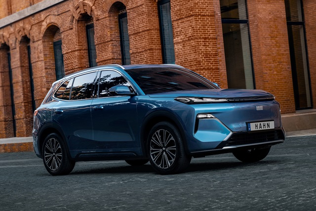 Seitenansicht eines blauen Geely Starray EM-i SUV vor einem Backsteingebäude mit großen Rundbogenfenstern