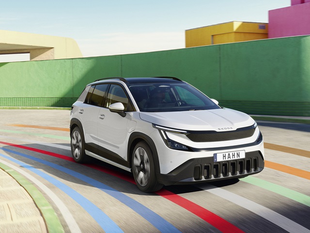 Weißer Skoda Epiq SUV von vorne mit schwarzem Kühlergrill und HAHN-Kennzeichen auf farbig markiertem Asphalt vor grünem und pinkem Hintergrund