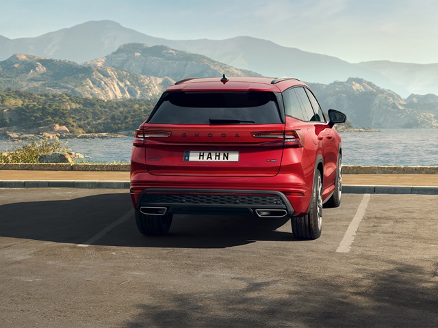Rote Škoda Kodiaq RS-Heckansicht mit getönten Scheiben und Doppelendrohr in einer Parklücke vor Berg- und Wasserlandschaft