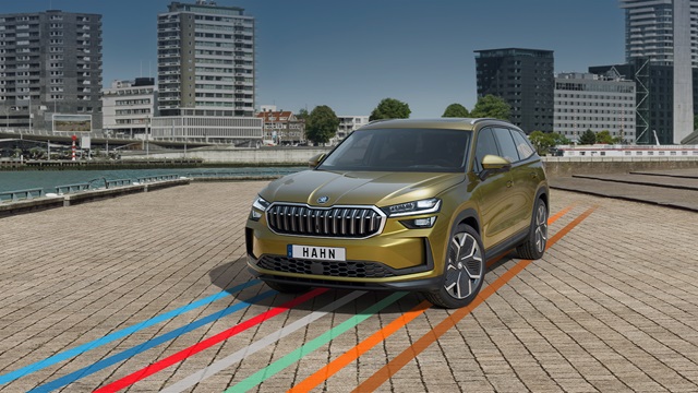 Škoda Kodiaq SUV in gelber Lackierung frontal auf gepflastertem Parkplatz mit mehrfarbigen Linien und städtischer Kulisse im Hintergrund