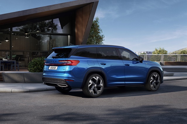 Blauer Škoda Kodiaq Sportline in Seitenansicht vor modernem Gebäude mit großen Fenstern und Holzverkleidung