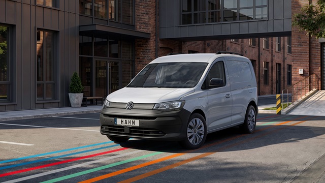  Weißer VW Caddy Cargo Kleintransporter frontal vor modernem Backstein- und Glasgebäude geparkt