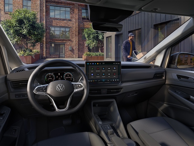 Innenraum des VW Caddy Cargo mit Lenkrad, digitalem Kombiinstrument und mittig angeordnetem Touchscreen vor urbaner Kulisse
